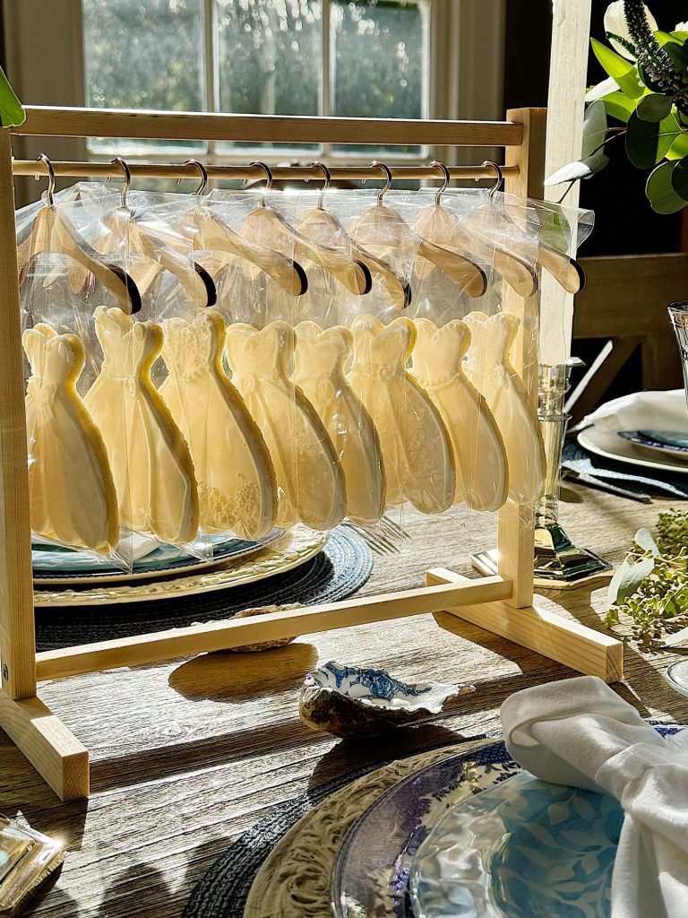 Cookies shaped as wedding dresses haging on a wooden rack in a sunlit dining room.