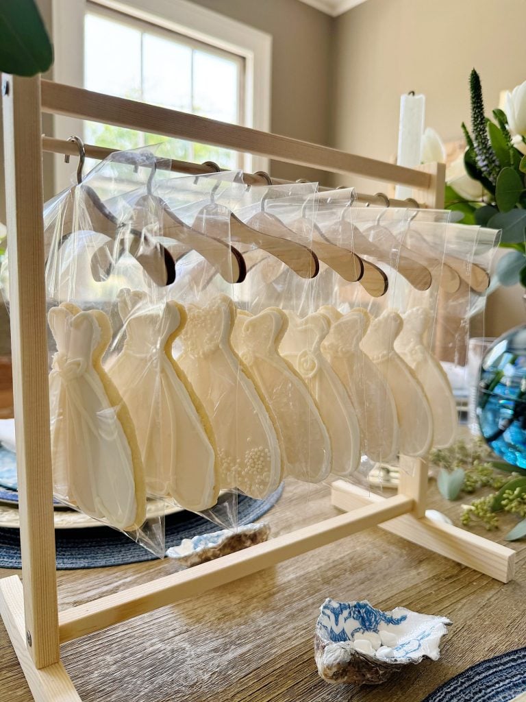 Wedding dress-shaped cookies in transparent bags displayed on a wooden stand as party favors.