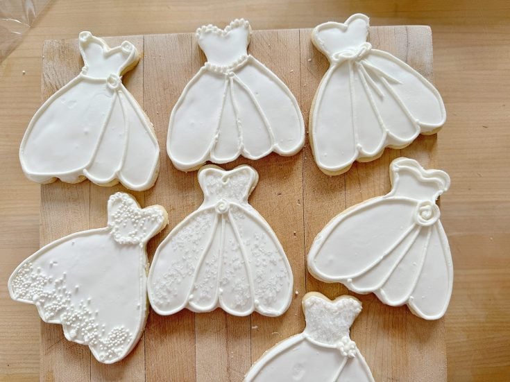 A collection of wedding dress-shaped cookies decorated with white icing on a wooden board.