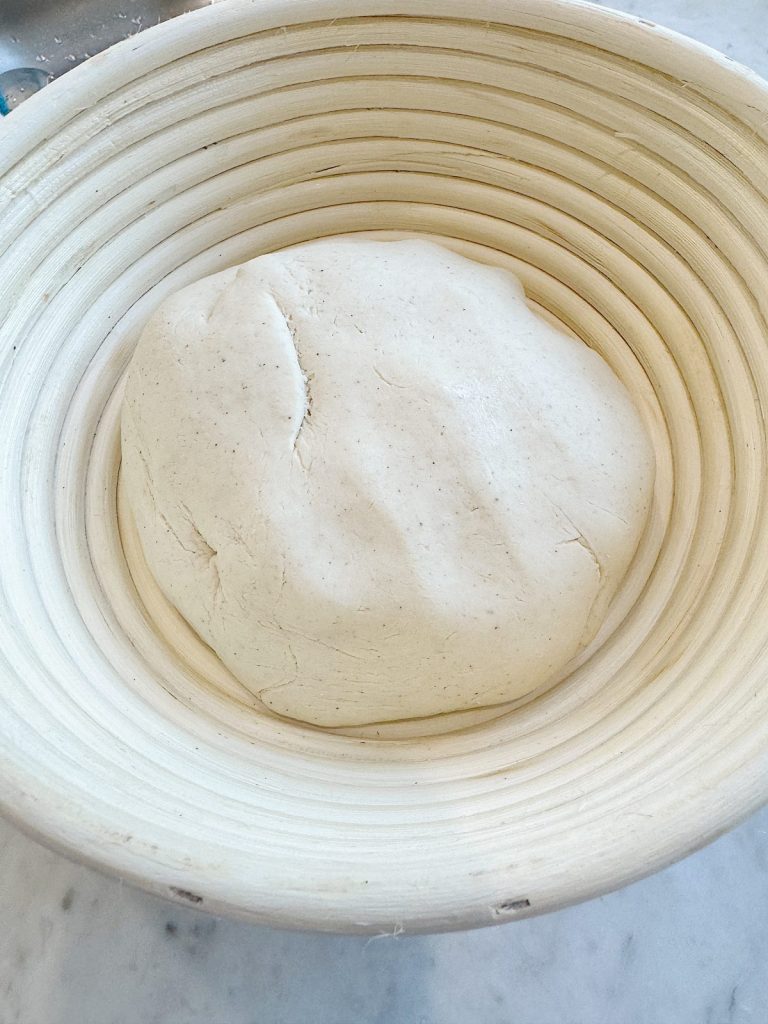 Unbaked pizza dough proofing in a floured banneton basket.