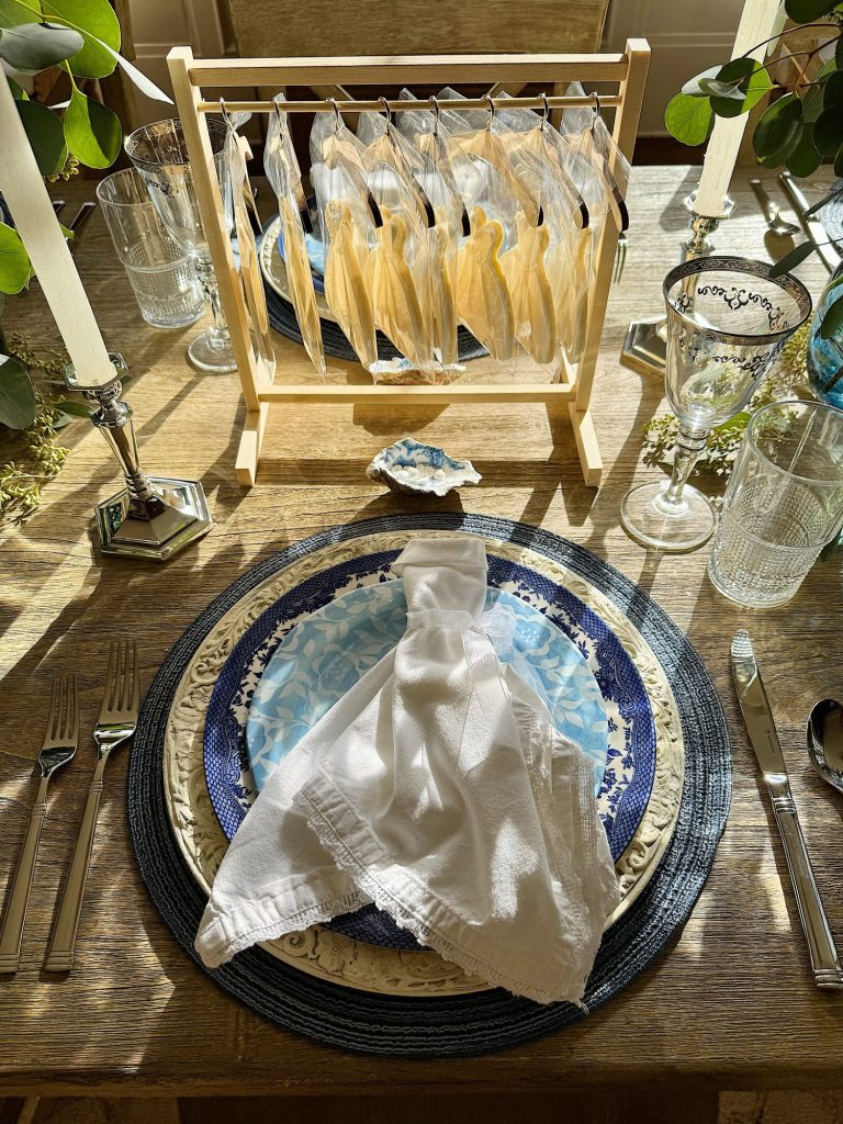 A sunlit dining table set with plates, cutlery, and adoll clothes rack with wedding gown shaped cookies in the background.