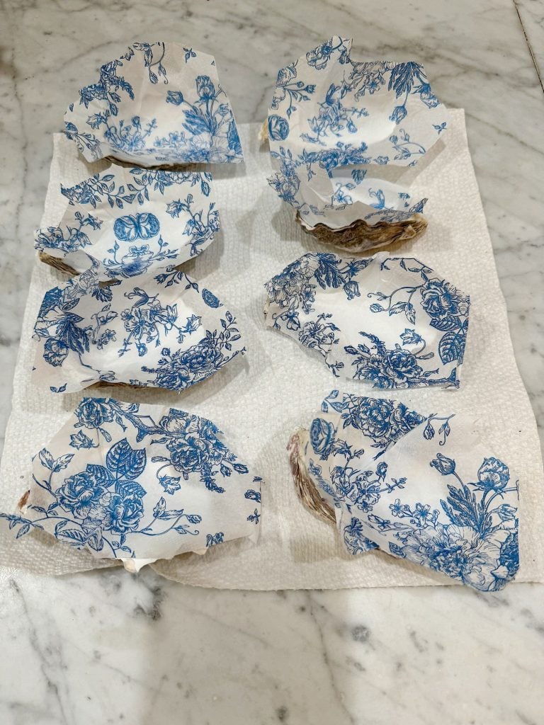 Blue and white paper napkins glued to the inside of oyster shells on a marble surface with paper towels.