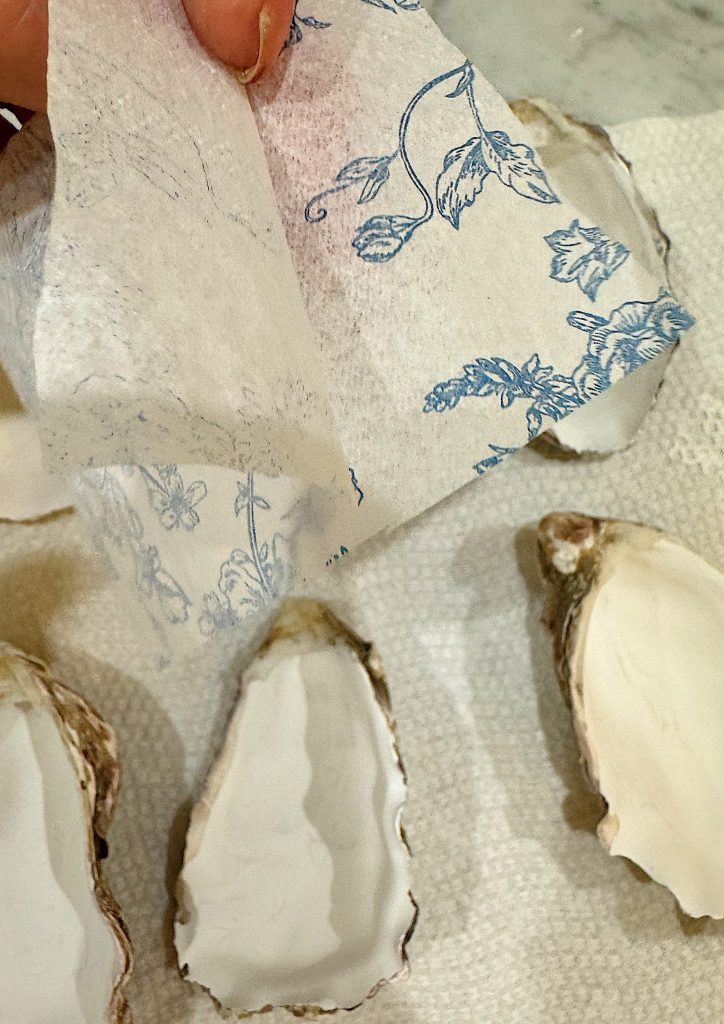 A person peeling off a floral design paper and oyster half shells on a countertop.