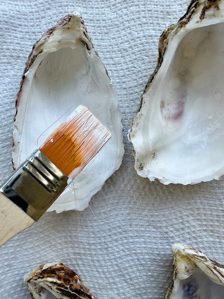 A paintbrush resting on a white textured surface beside two empty oyster shells.