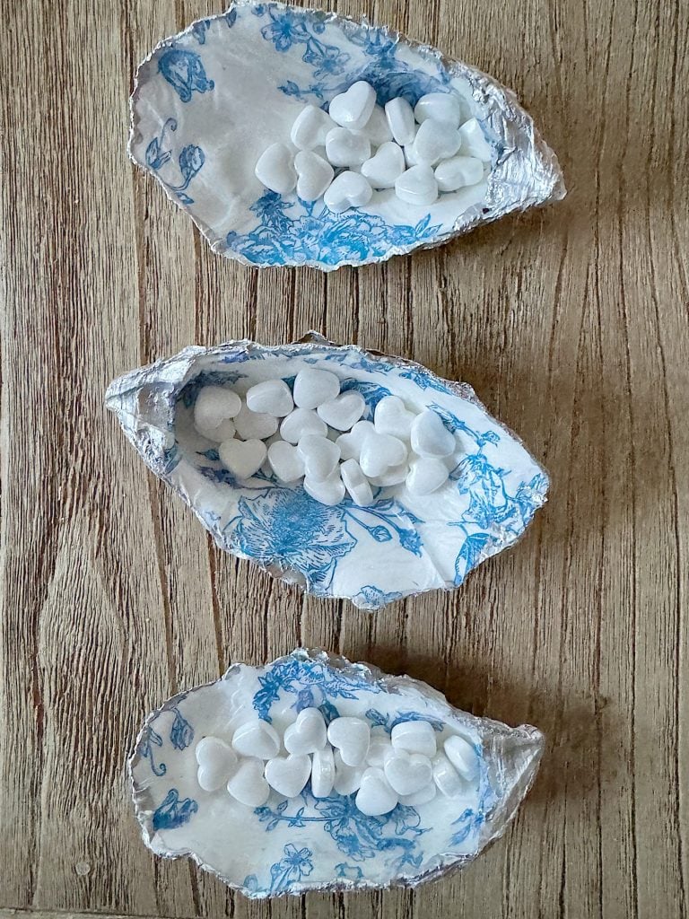 Three decorative oyster shells with a blue and white floral design, filled with white candies, arranged on a table.