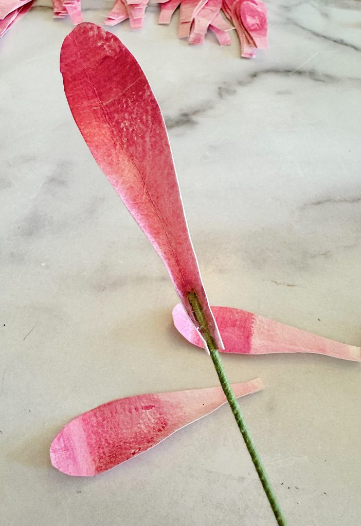 Two pink paper petals on a marble surface, one standing upright and the other one lying flat.