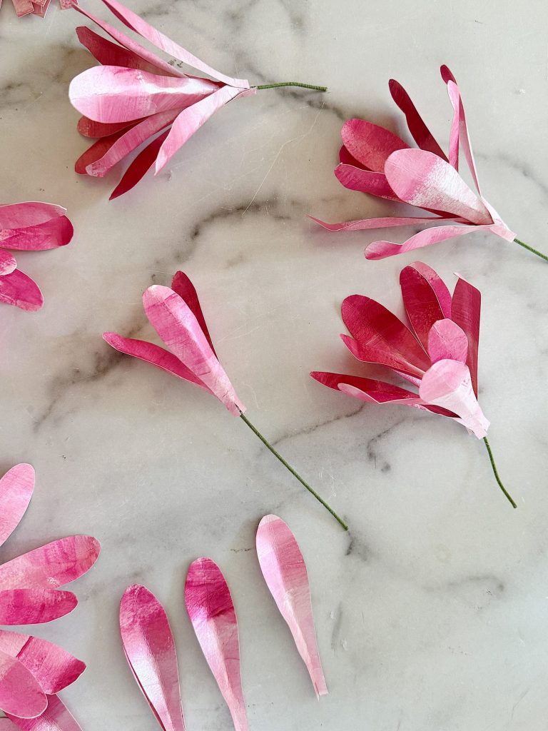 Pink paper made from paper flowers scattered on a marble surface.