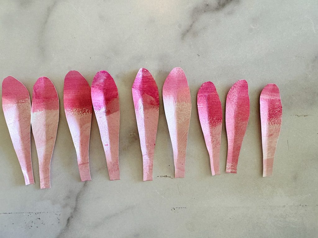 Nine pink petals made from paper arranged in a row on a marble surface.