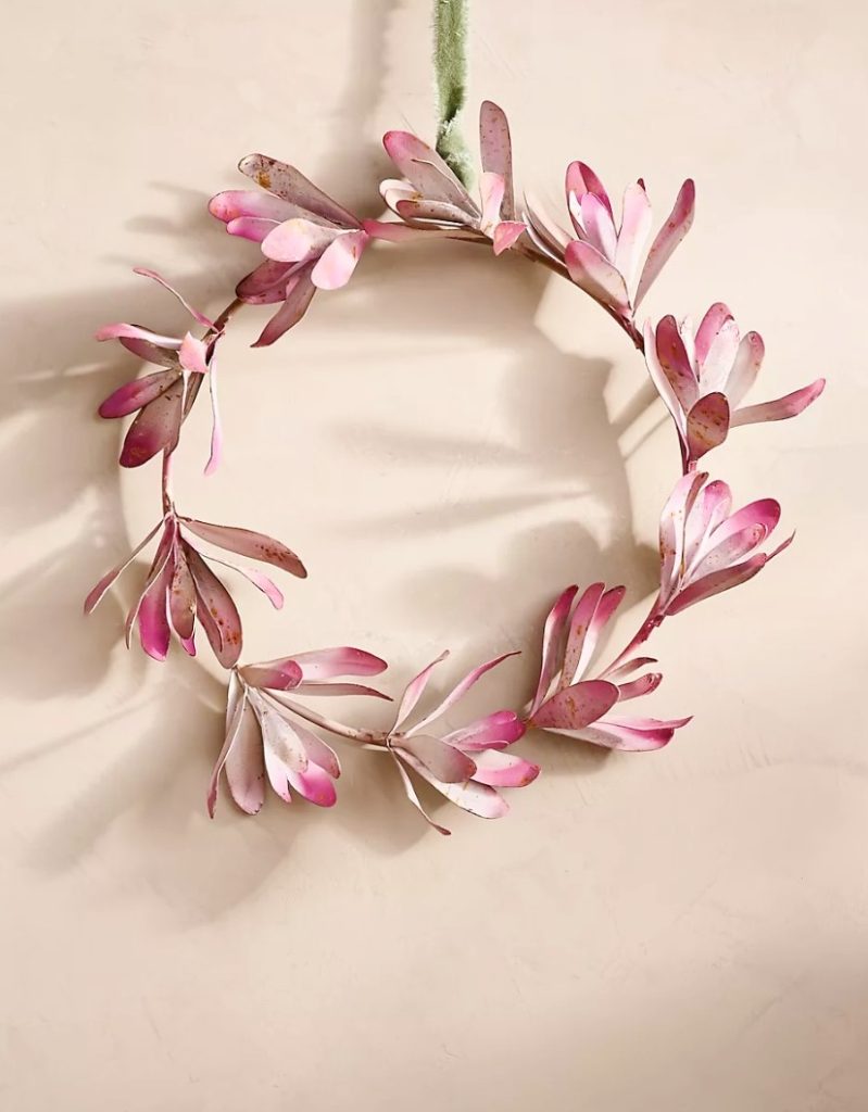 A decorative wreath with pink petals arranged in a circular pattern hanging against a pale background.