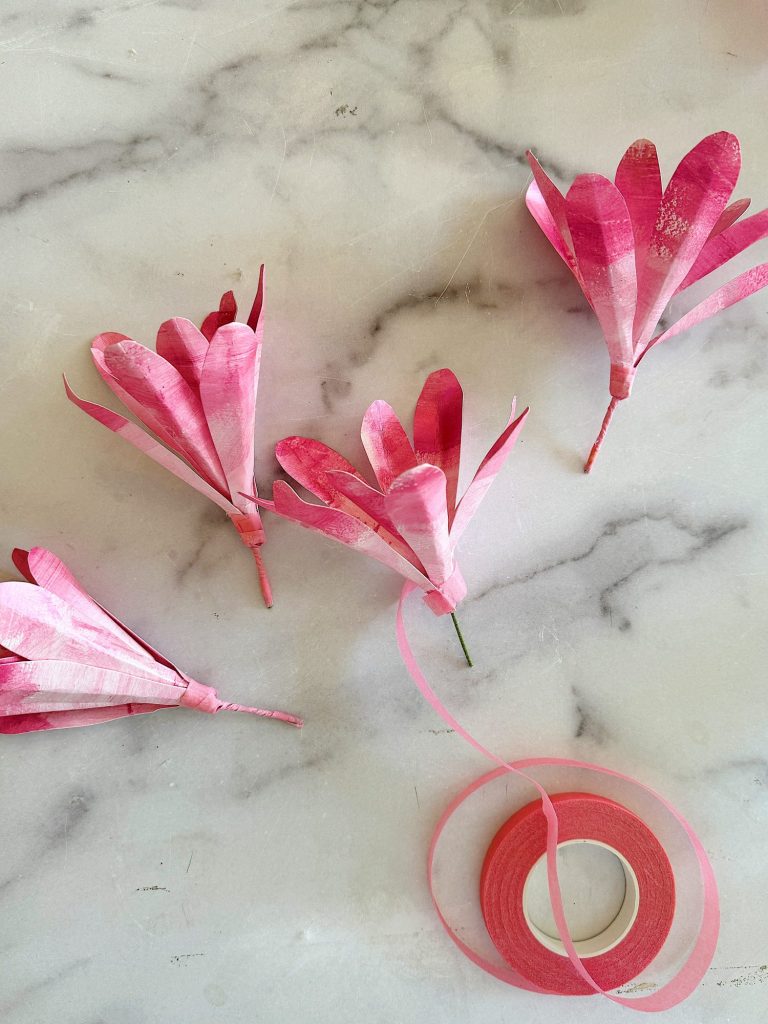 Pink paper tulips crafted with floral tape on a marble surface.