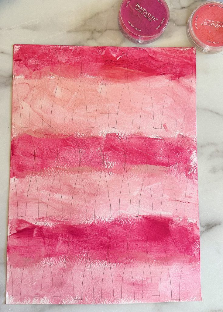 A piece of paper with abstract pink and light pink paint strokes on a marble surface.