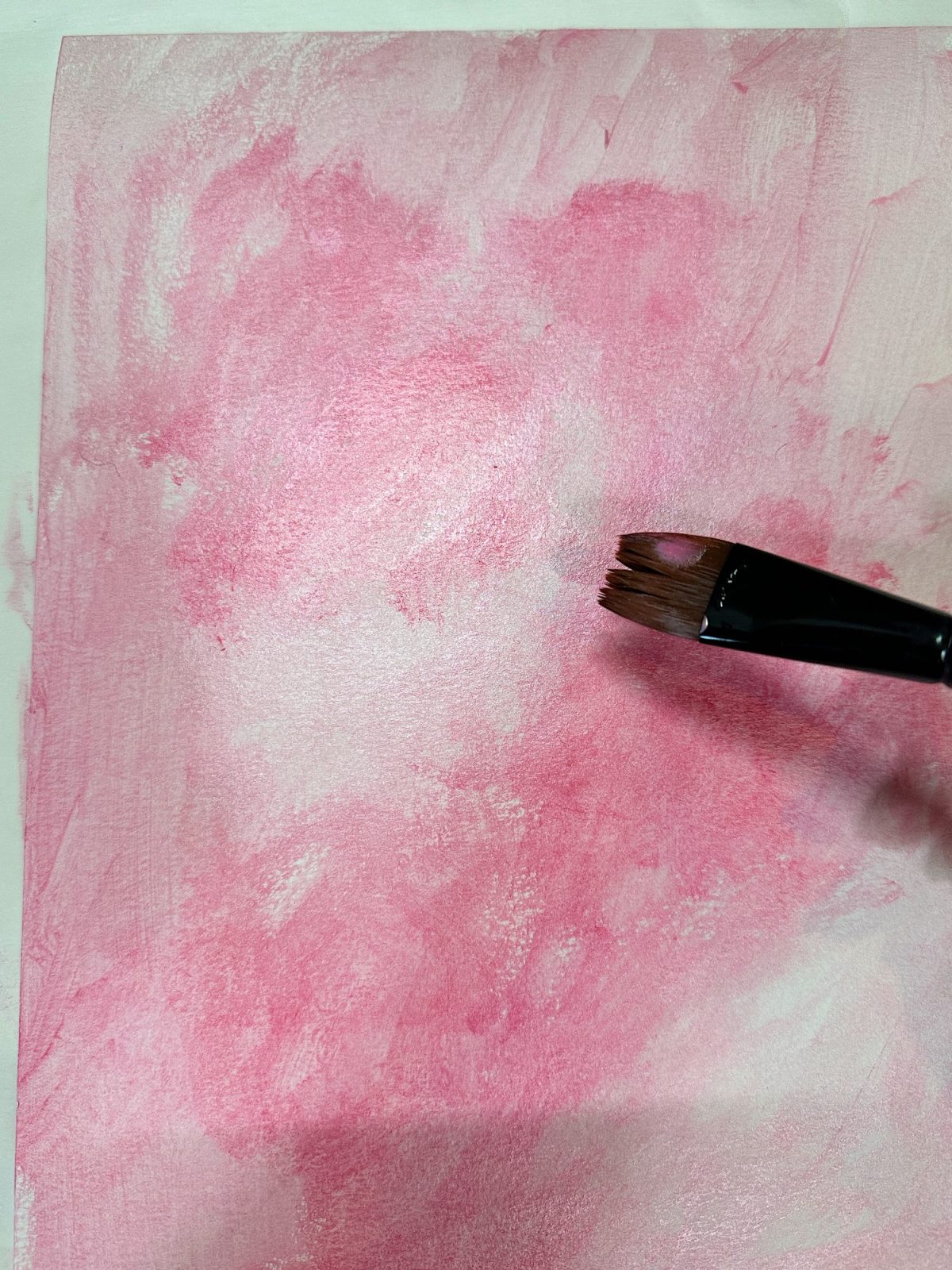 A piece of paper with abstract pink and light pink paint strokes on a marble surface.