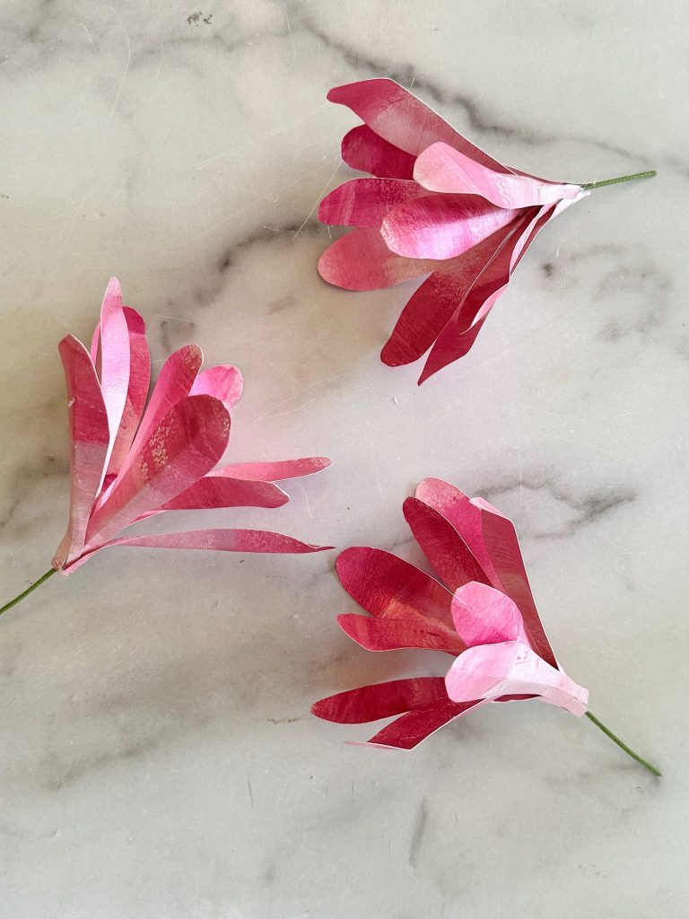 Three pink and white paper pink magnolia flowers on a marble surface.