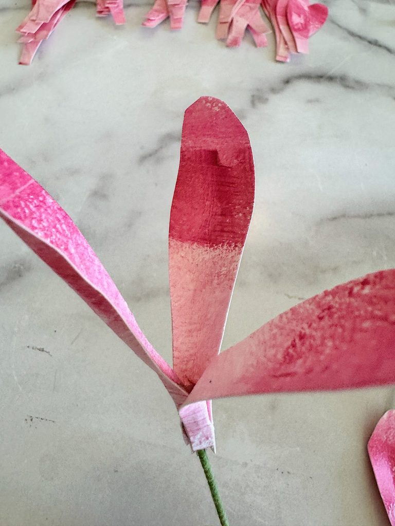 A paper pink magnolia flower with a green stem on a marble surface.