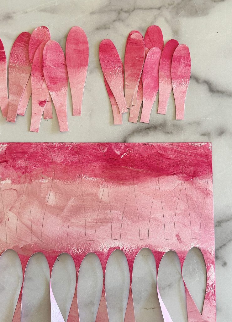 Cutting pink paper into petals with scissors on a marble surface.