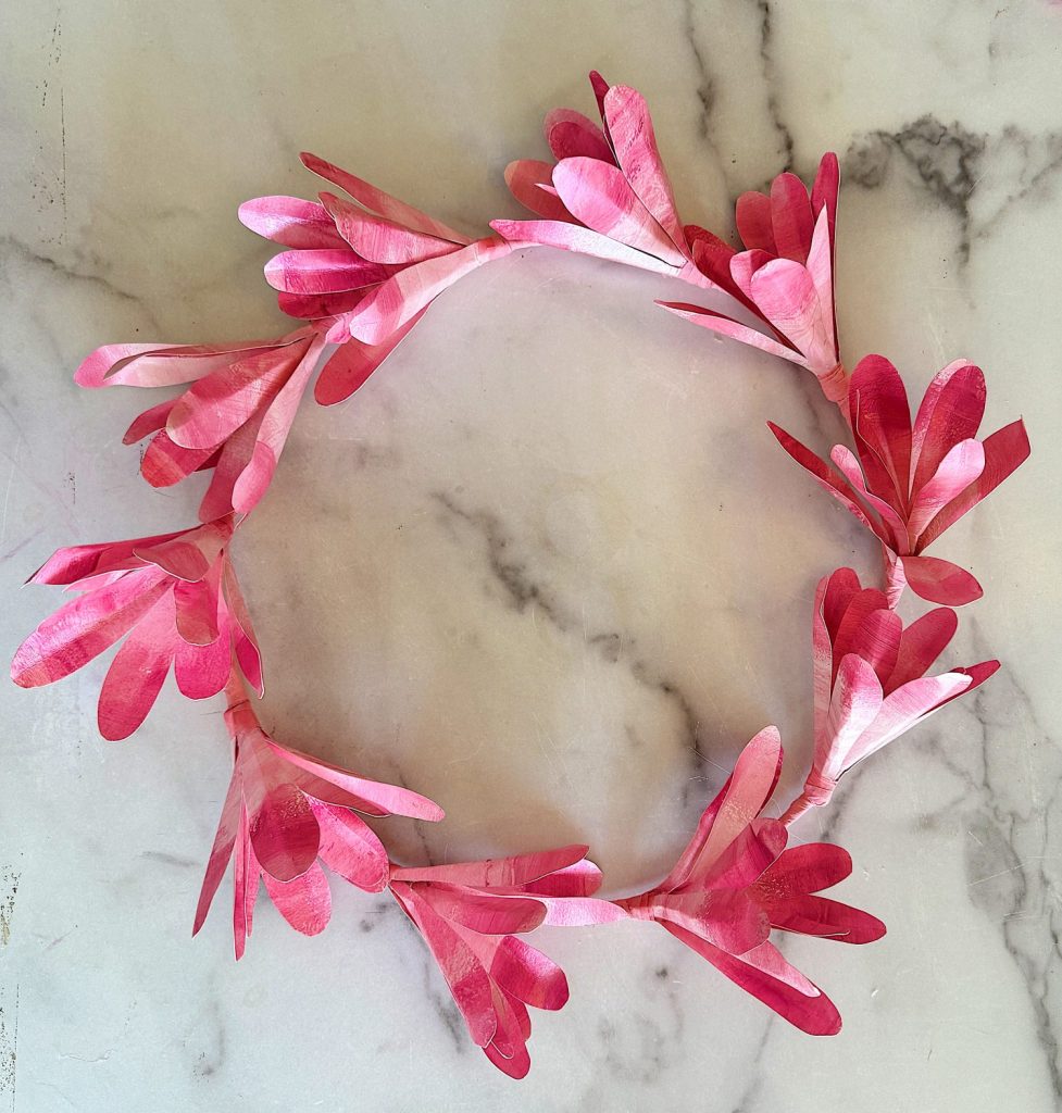 A pink magnolia tree flower wreath made from paper on a marble surface.