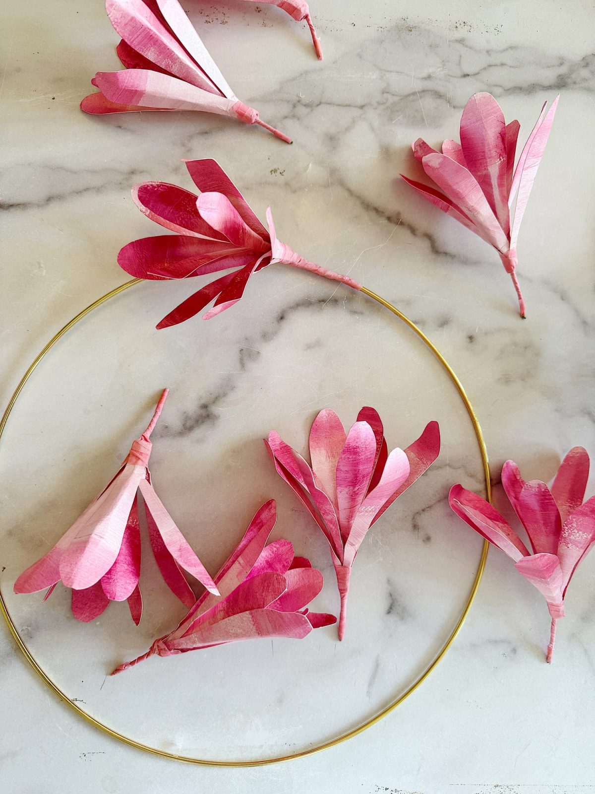 Pink magnolia tree paper petals arranged in a circular pattern on a marble surface.