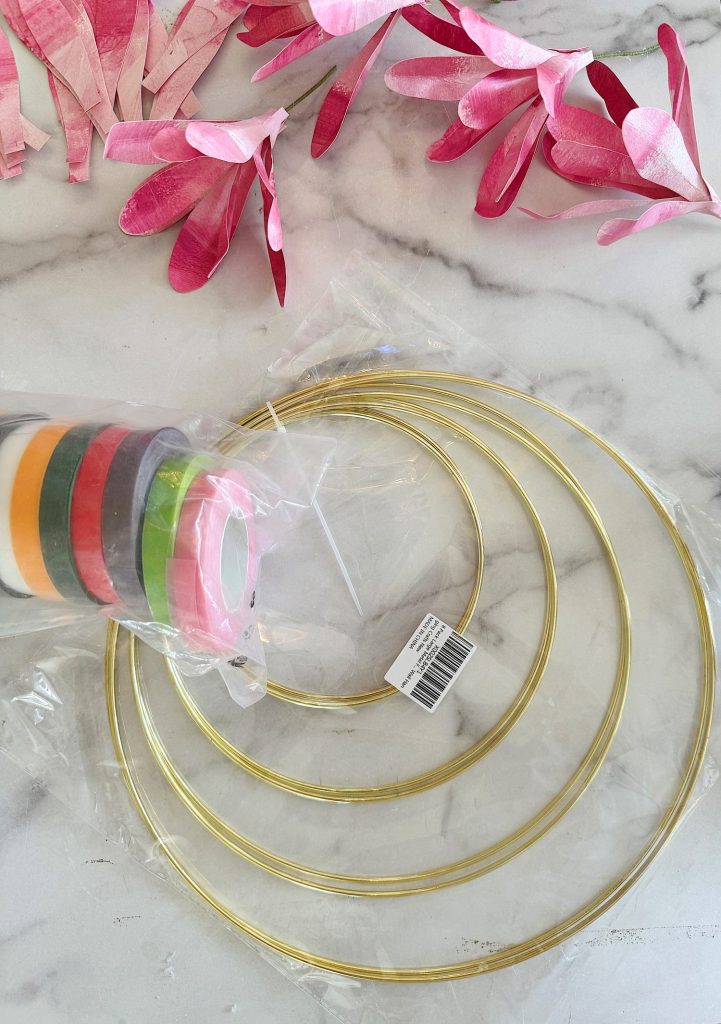 Crafting materials including metal rings and colorful tape on a marble surface with pink foliage.