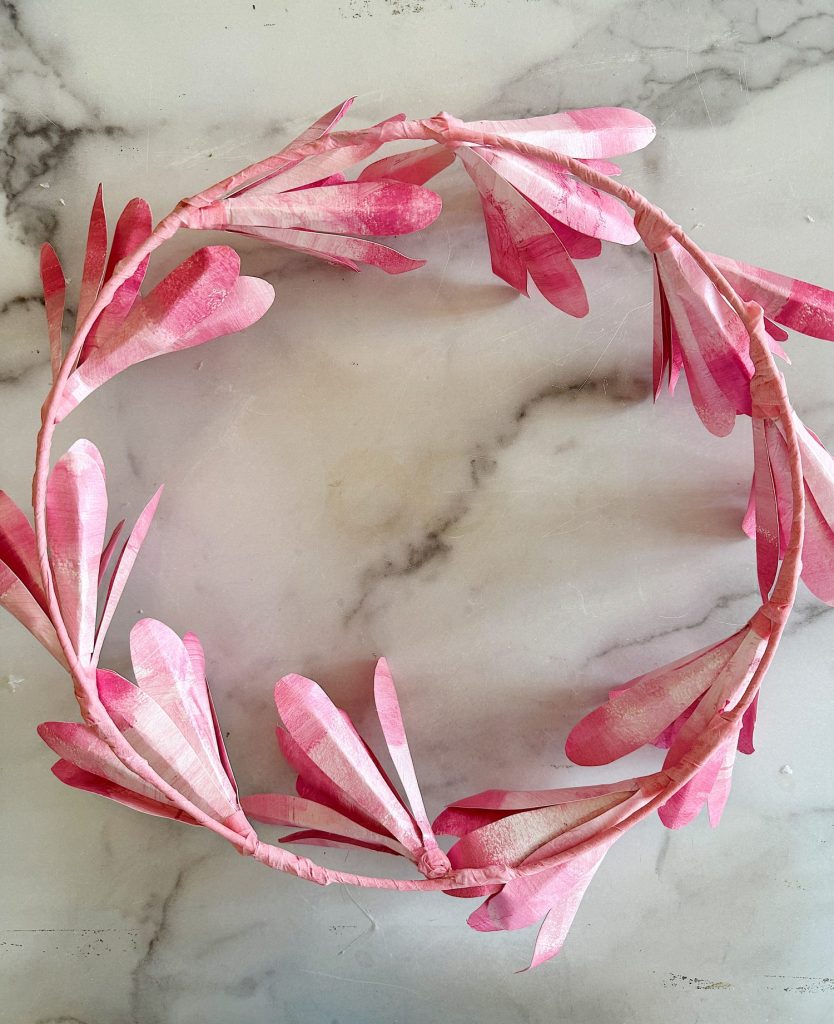 A pink magnolia tree flower wreath resting upside down on a marble surface.