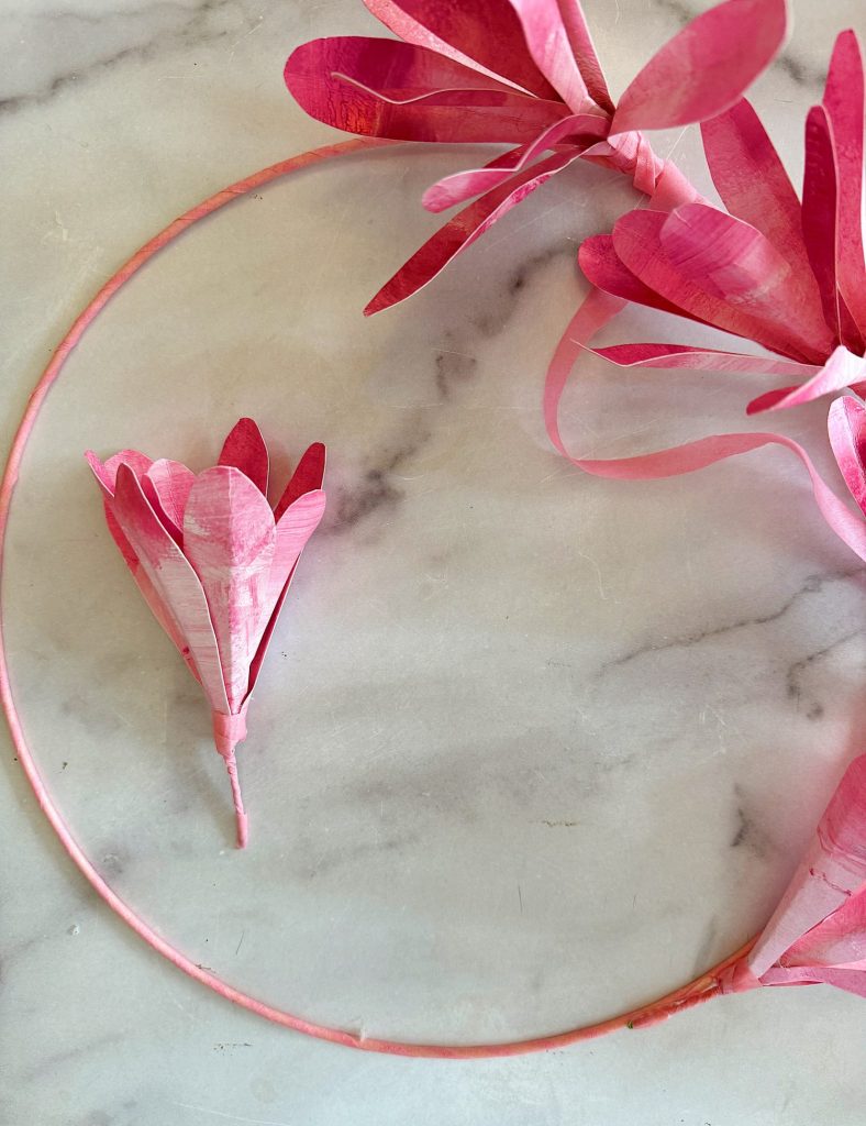 A pink floral wreath made from paper on a marble surface.