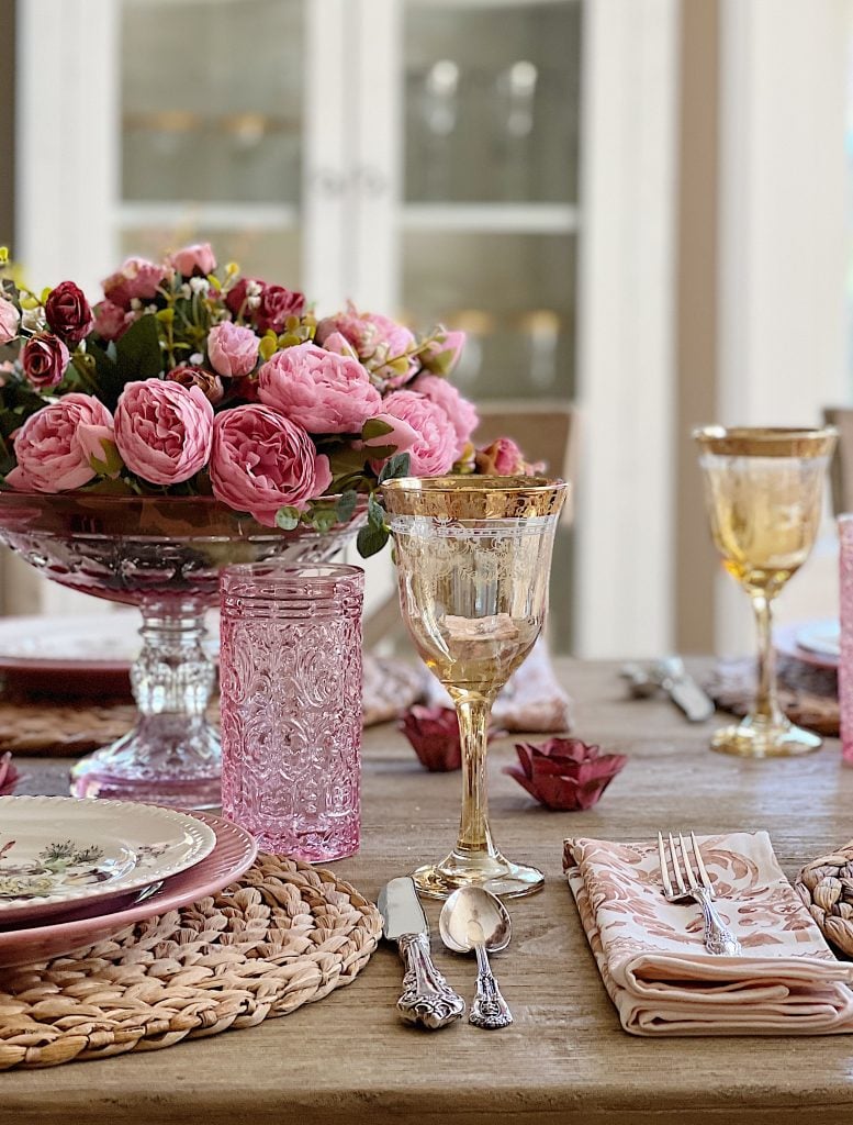Elegant table setting with pink roses centerpiece, vintage glassware, and patterned china.
