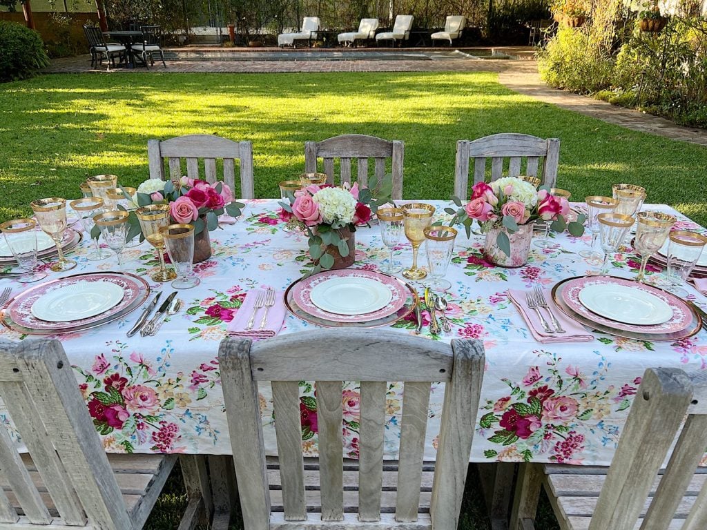 Elegant outdoor dining setup with floral tablecloth and rose centerpieces.