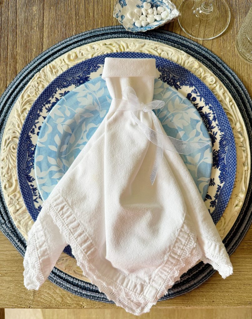 An elegantly folded white napkin resembling a wedding gown, presented on a table set with decorative blue and white plates.