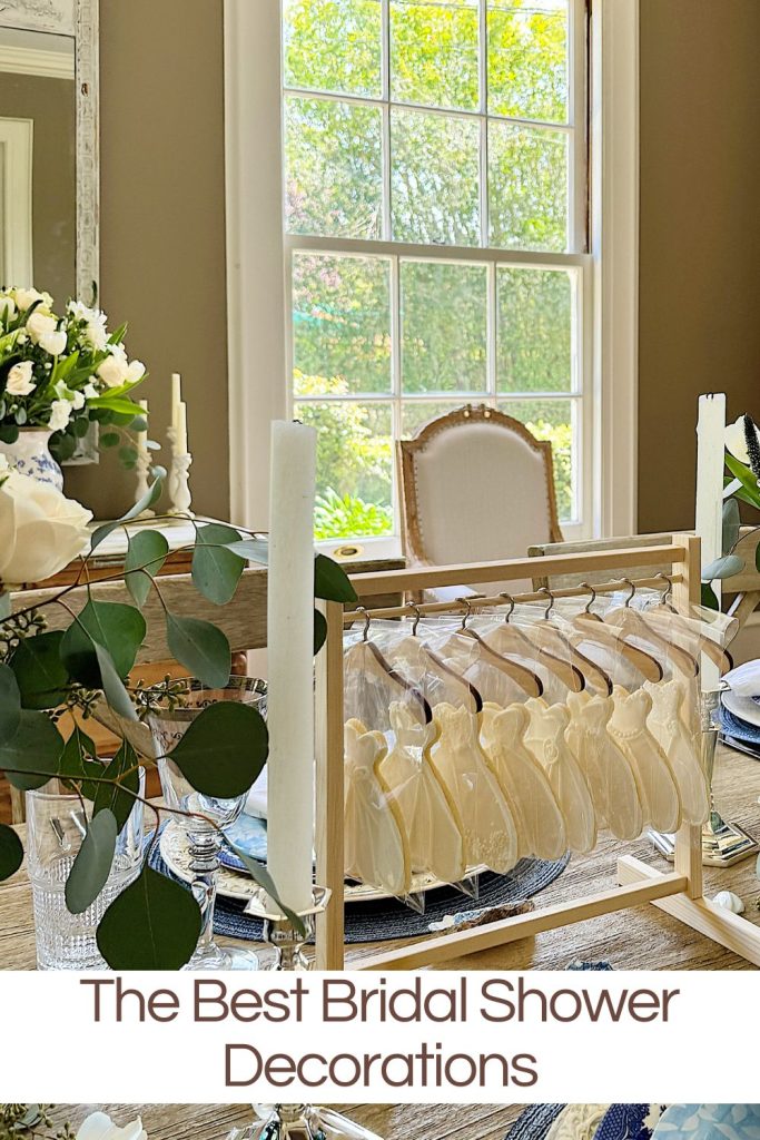 Elegant bridal shower setup with a miniature wooden clothing rack displaying white wedding dress cookies and a bouquet of flowers on the table.