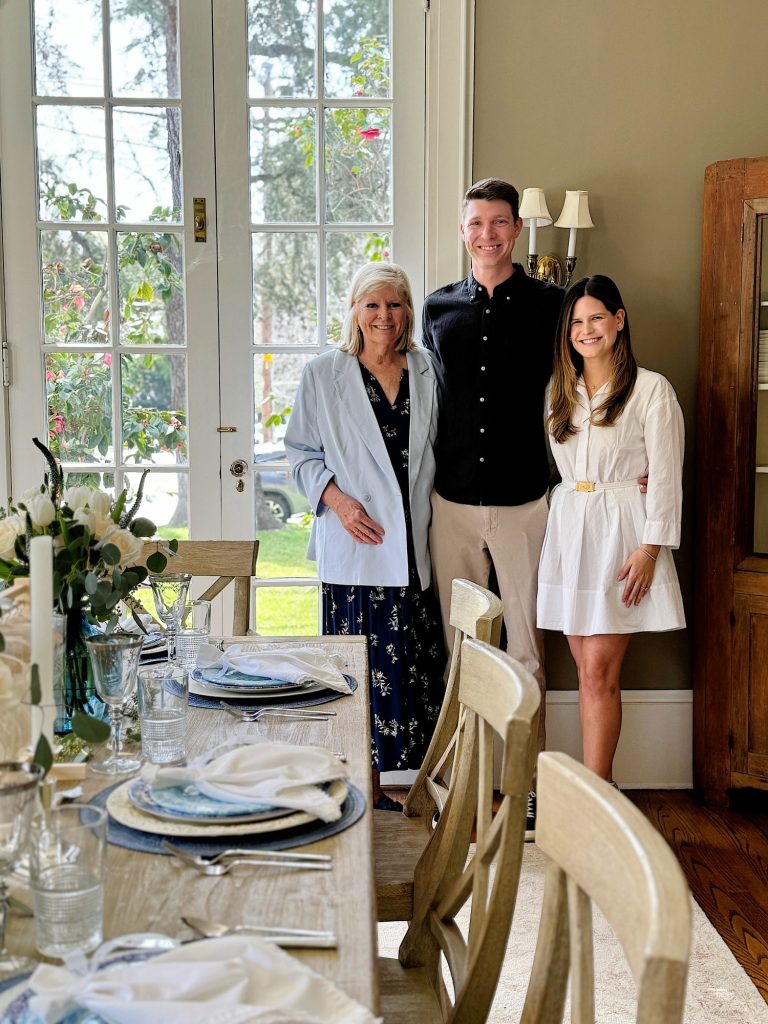 Three people standing together smiling in a dining room with a set table.