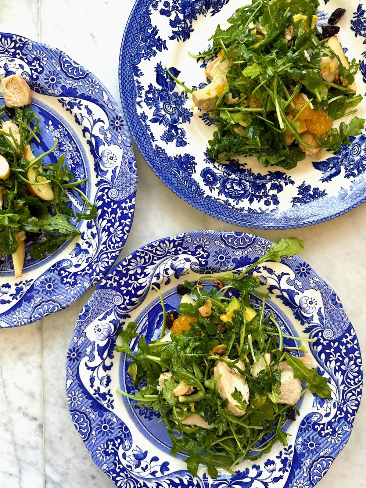 Three plates with green salads on a marble surface.