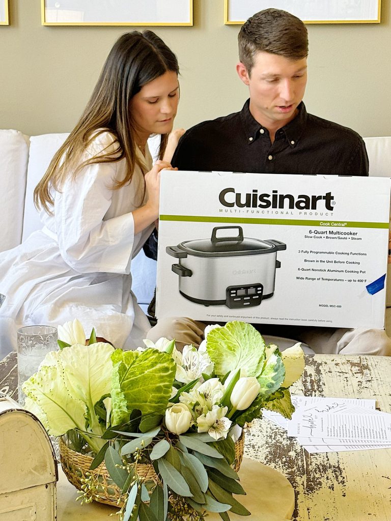 Two people examining a cuisinart multicooker box on a table with decorative flowers.
