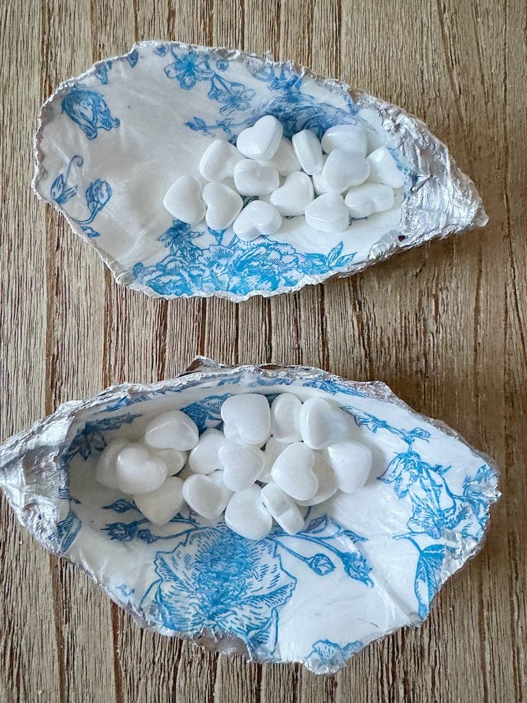 Two halves of a decorative oyster shell with vintage blue floral pattern, containing white decorative pebbles.