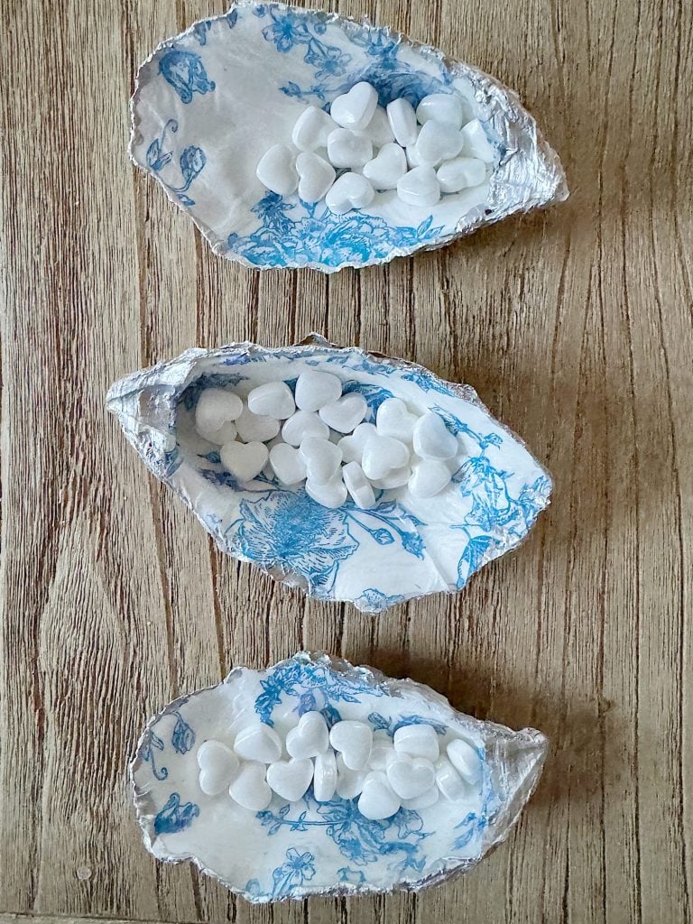 Three decorative oyster shells, each filled with small white candies, arranged on a wooden surface.