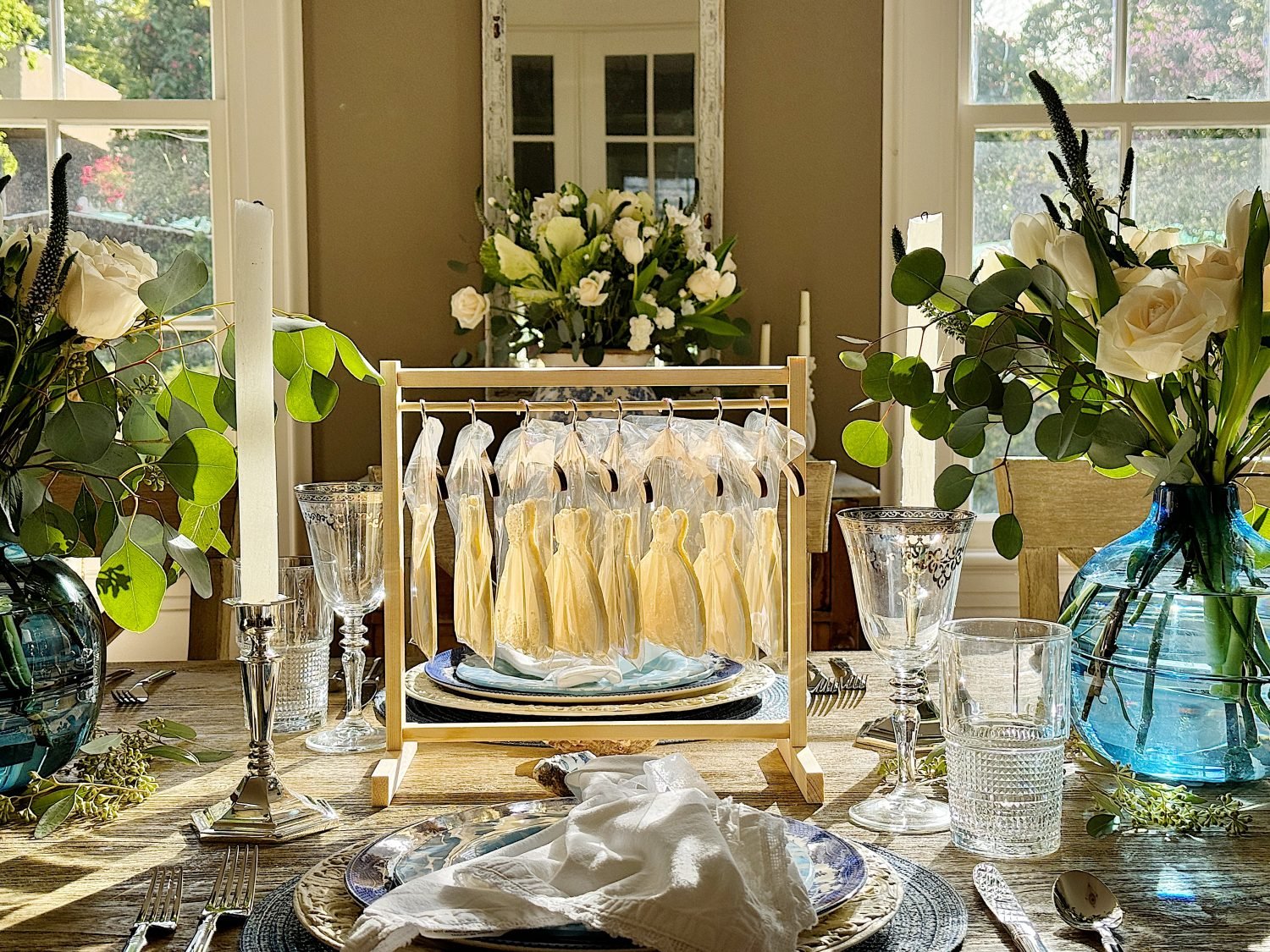 Elegant dining table set with glassware, flowers, and candles in a sunlit room.