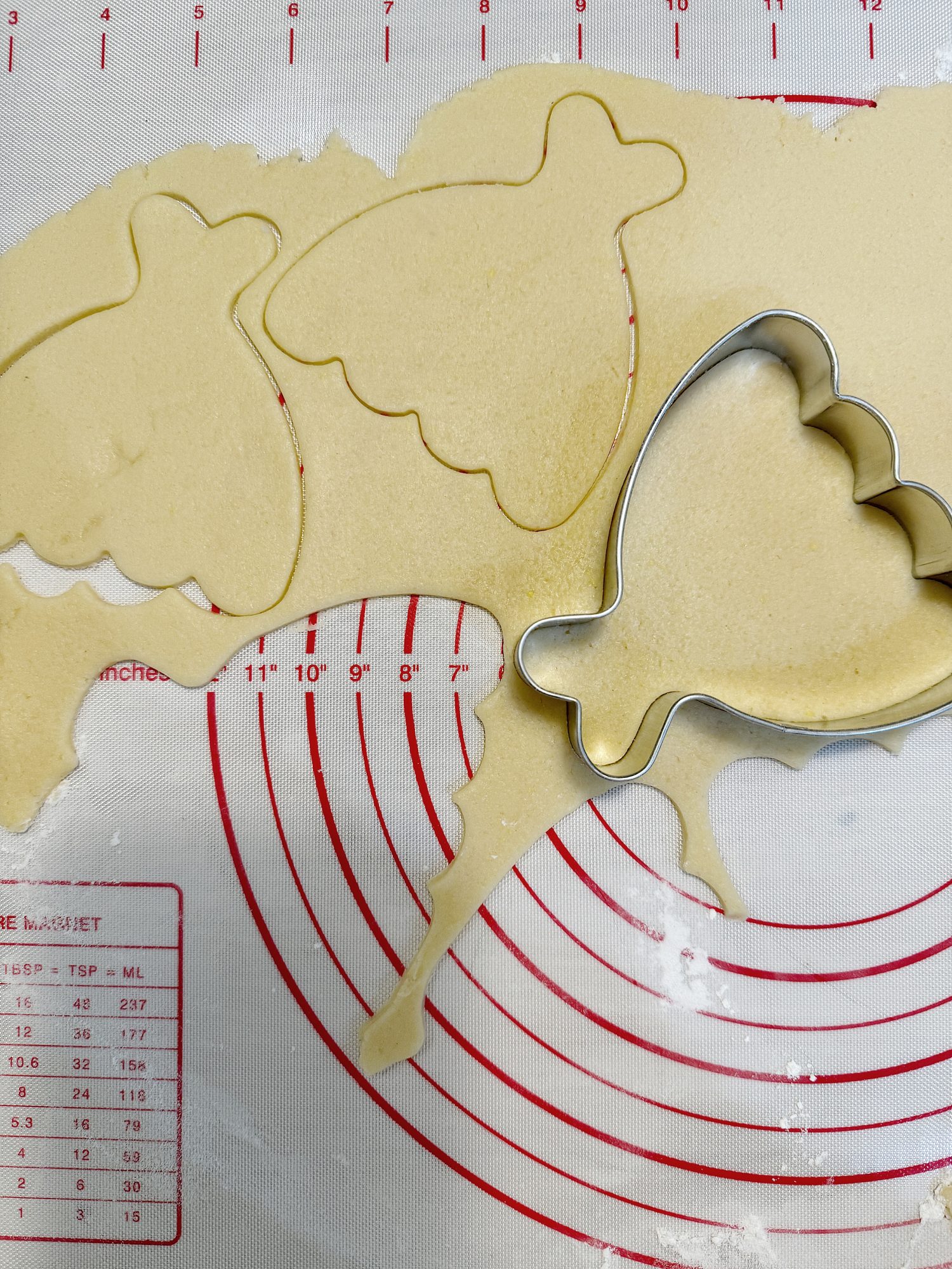 Rolled out cookie dough with a wedding dress-shaped cookie cutter and cut-out shapes.