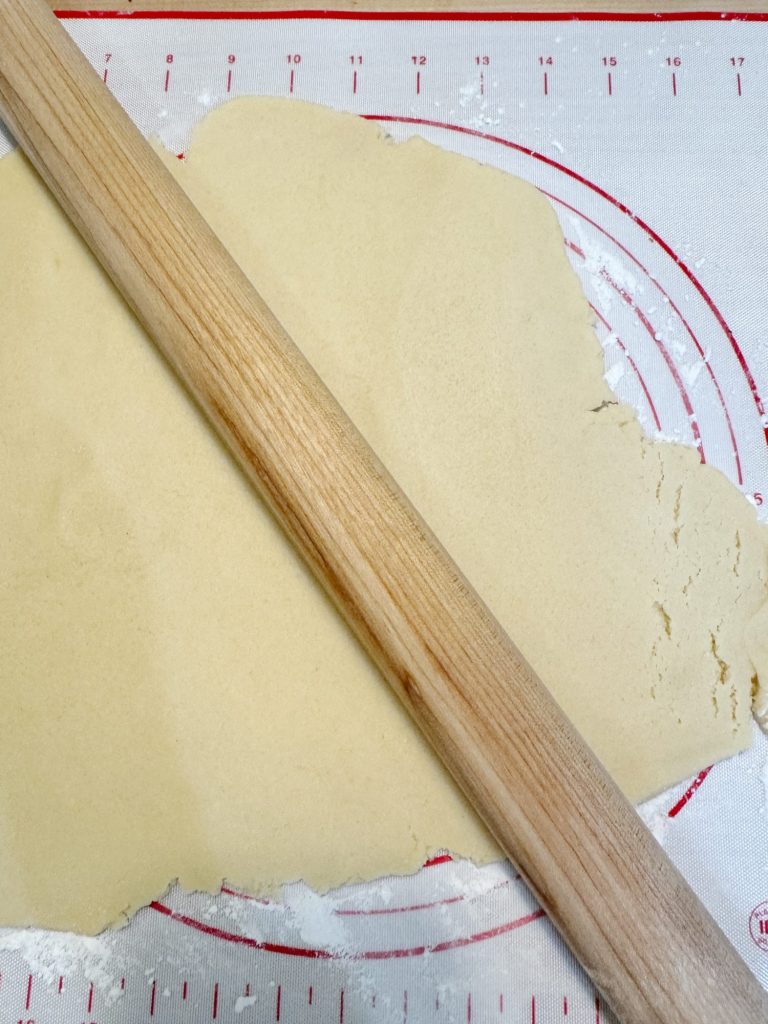 Rolled out dough with a rolling pin on a mat with measurement markings.