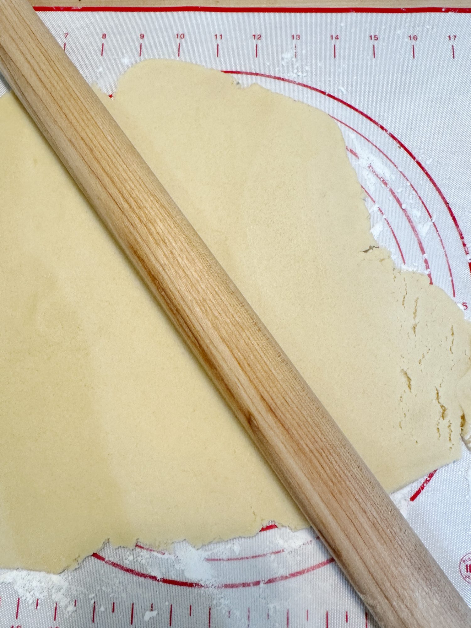 Rolled out dough with a rolling pin on a mat with measurement markings.