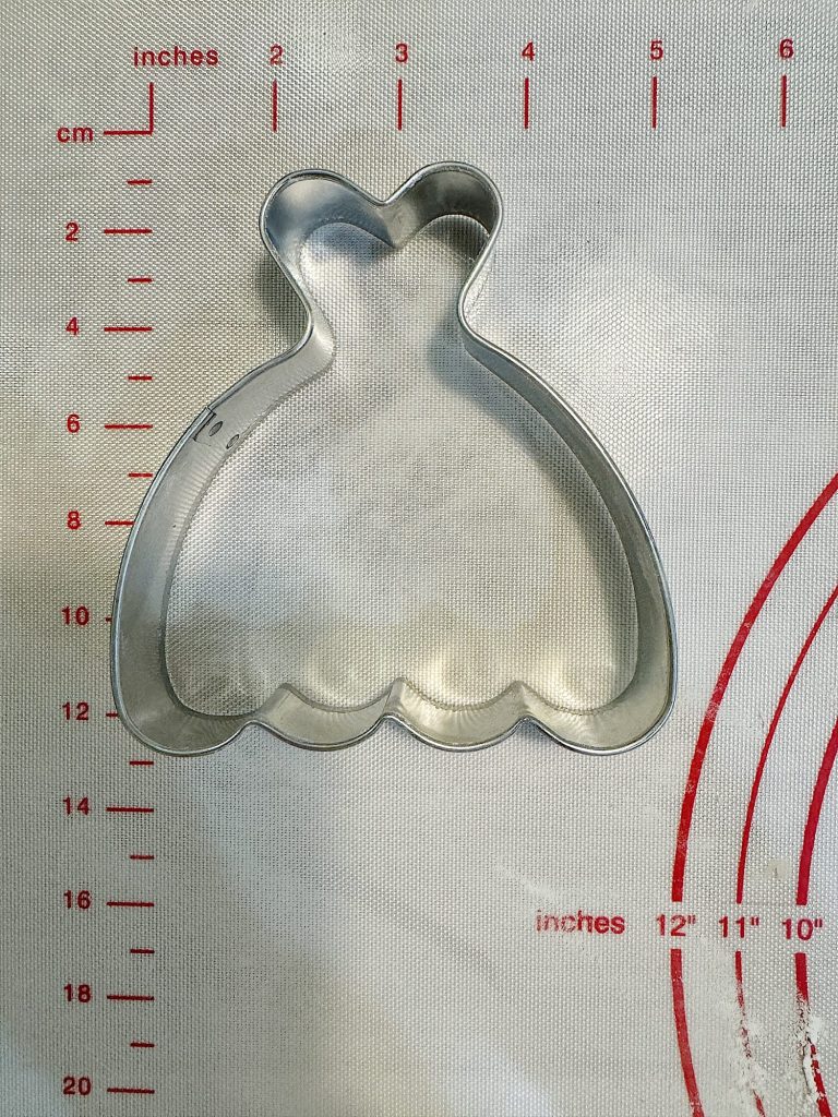 Metal cookie cutter in the shape of a wedding dress on a measuring mat.