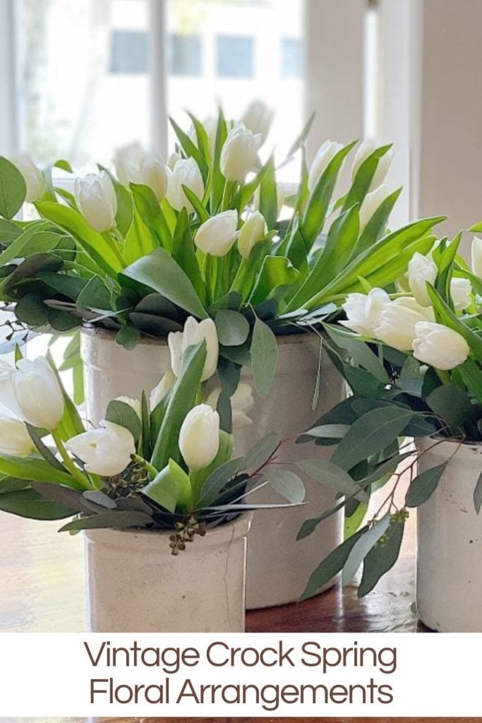 White tulips arranged in vintage crock pots on a table.