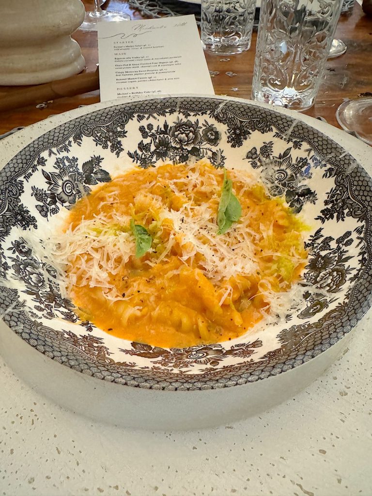 A bowl of ravioli topped with tomato sauce, grated cheese, and basil leaves, served on a decorative plate with a menu in the background.