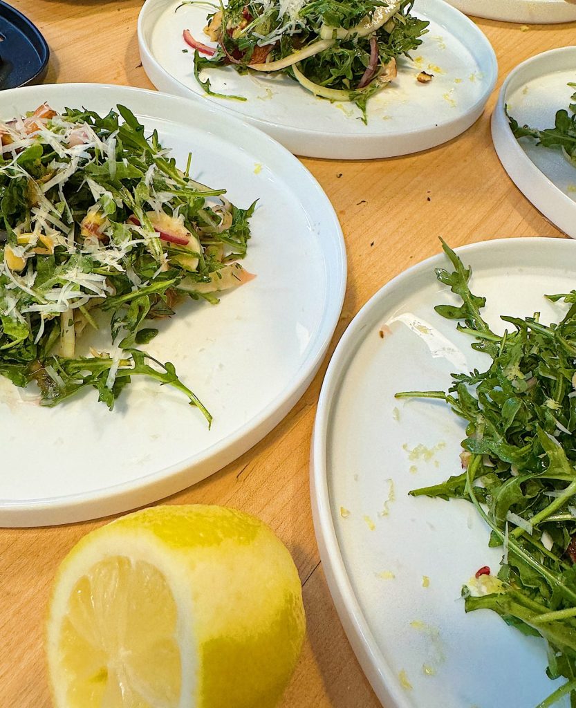 A table with plates of partially eaten salads and a sliced lemon in the foreground.
