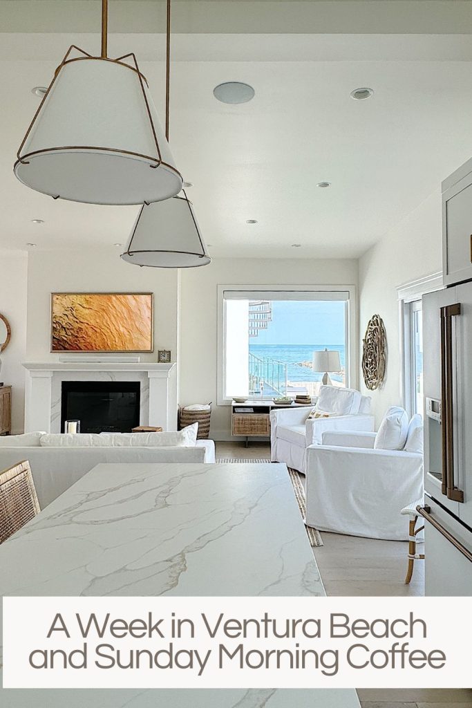Modern beachfront living room with white sofas, a marble countertop, a fireplace, and ocean view visible through large windows.