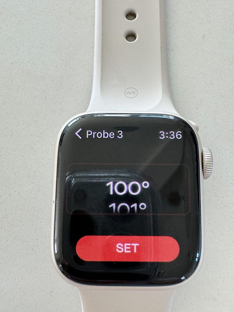 Close-up of a smartwatch with a display showing "probe 3" at the top, the time as "3:36", and numbers "100" and "1010" above a red "set" button.