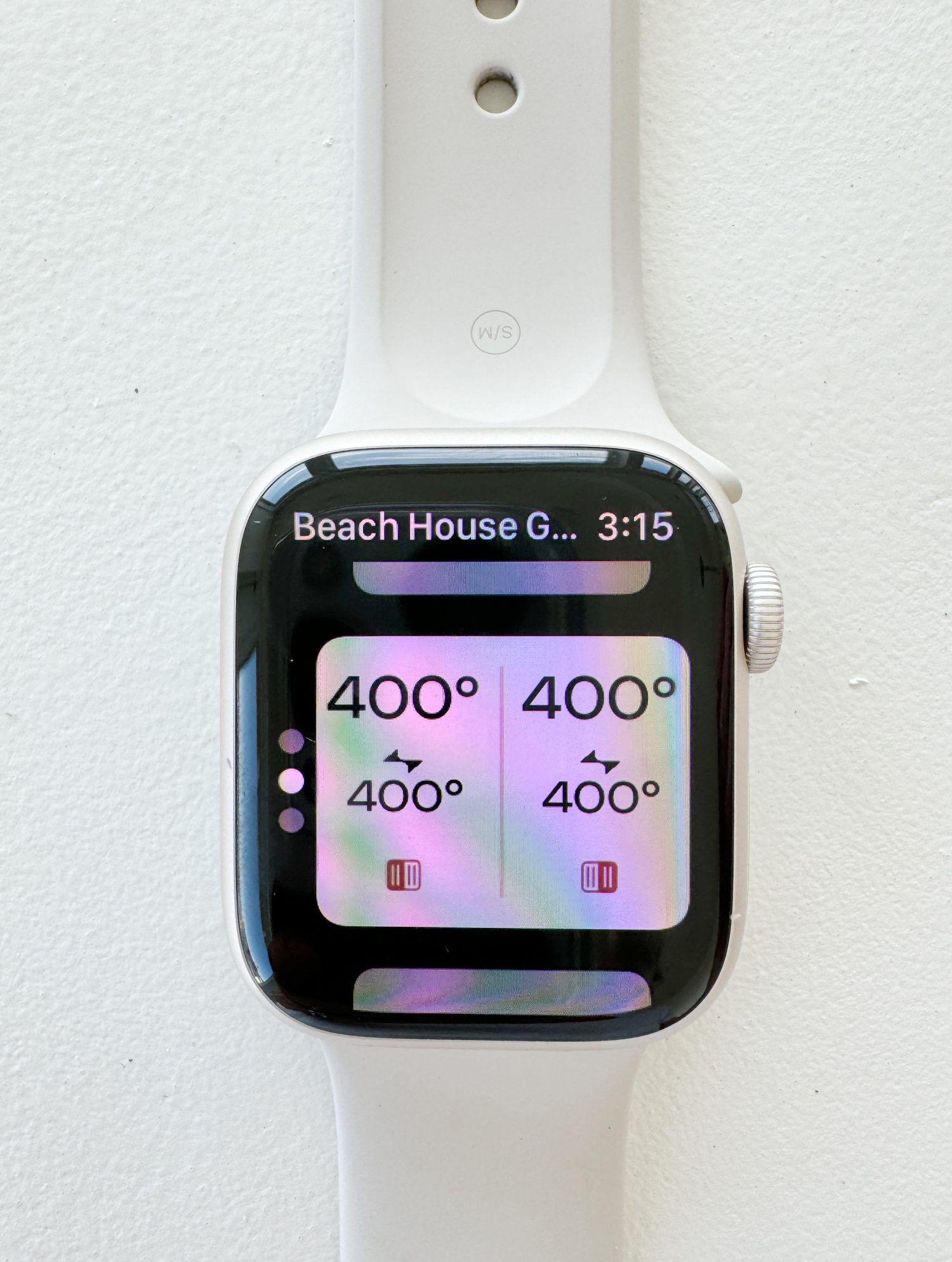 White smartwatch displaying colorful screen with four "400&deg;" temperature graphics, attached to a white band against a white wall.