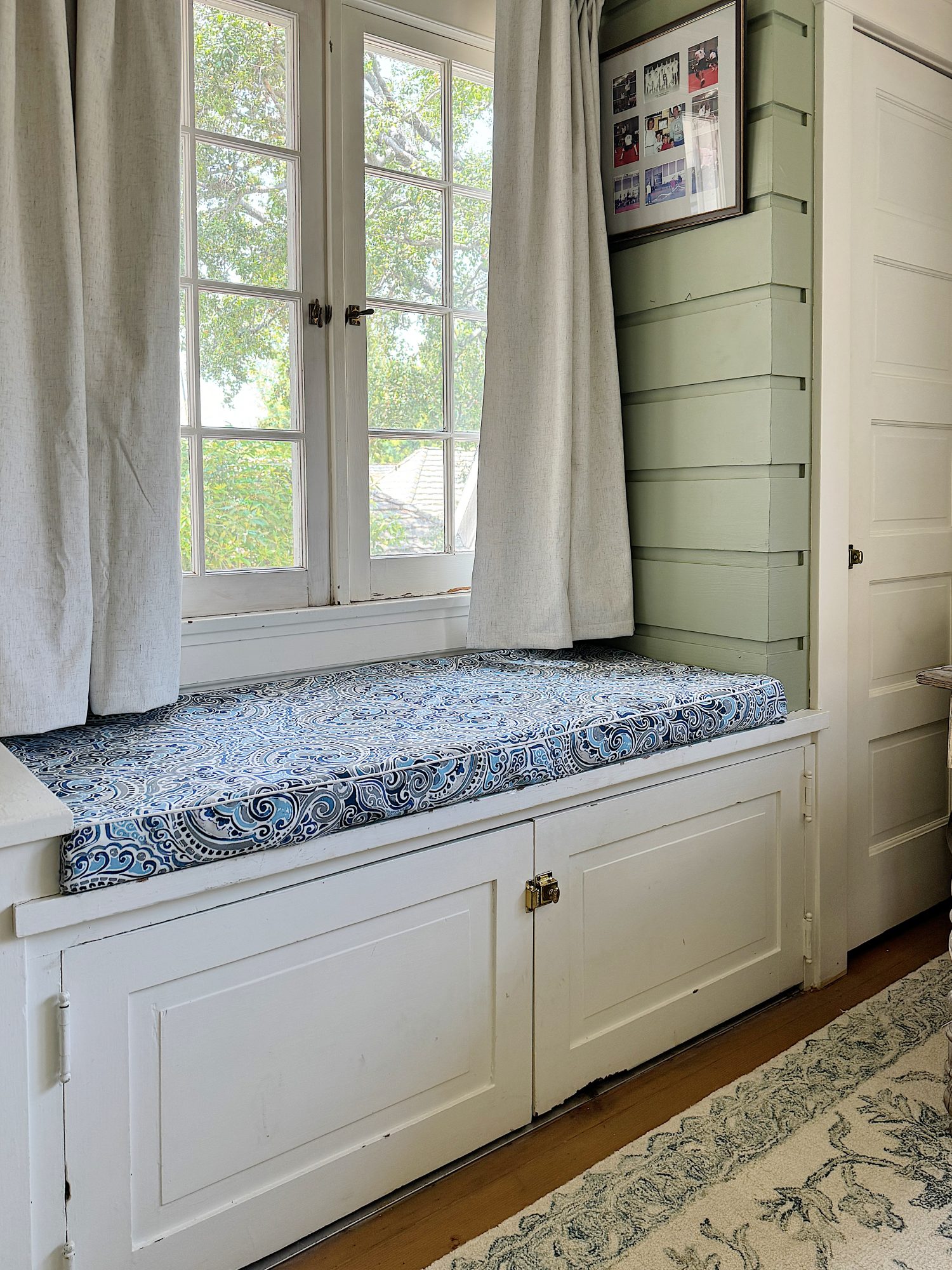 A cozy nursery with a white crib on the right, a rustic wooden table with baskets underneath by a window, and soft green walls.