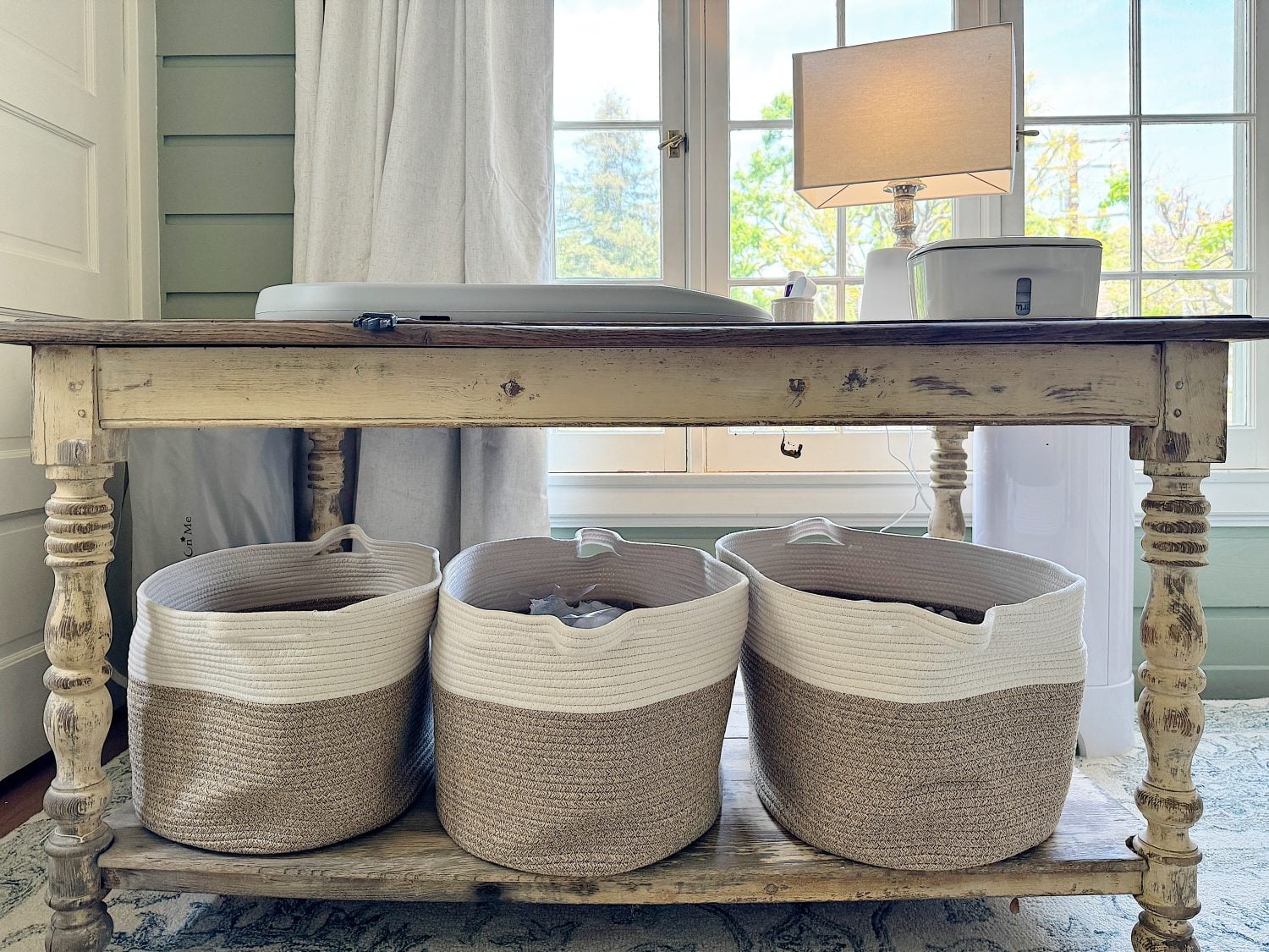 A cozy nursery with rustic wooden table with baskets underneath by a window.