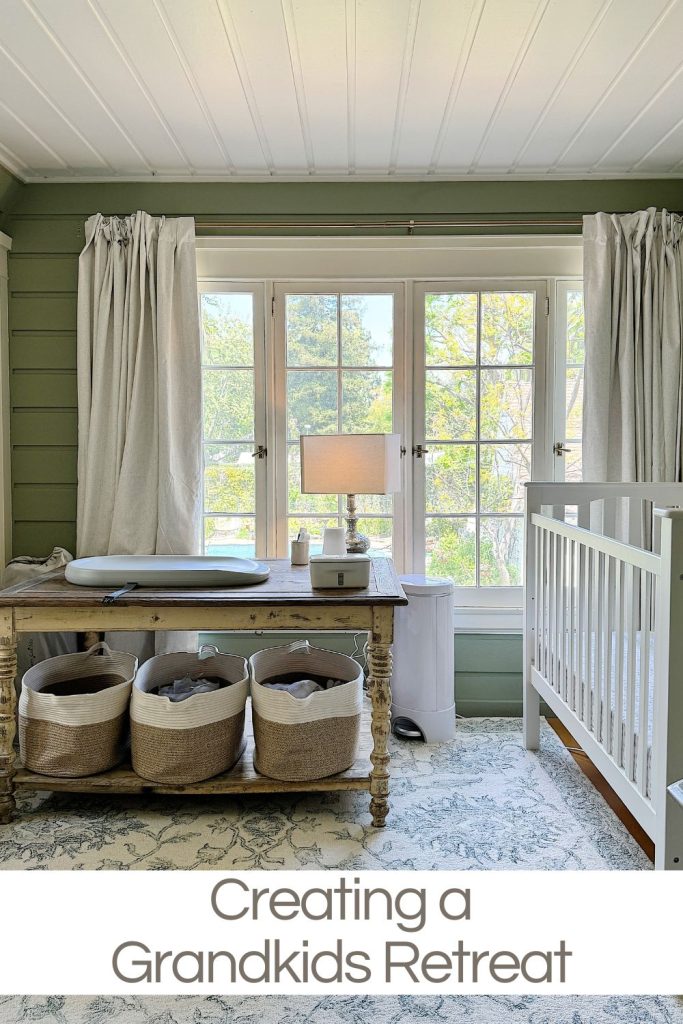 Cozy nursery room with a white crib, a desk with a lamp, storage baskets, and large windows with curtains, titled "creating a grandkids retreat.