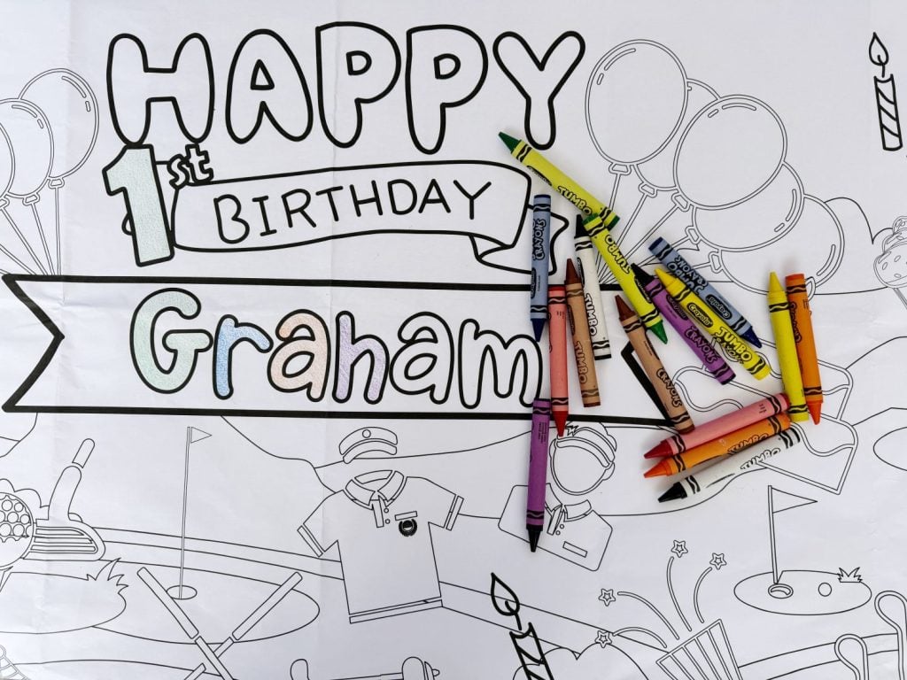 Coloring materials scattered on a personalized "happy 1st birthday graham" coloring banner.