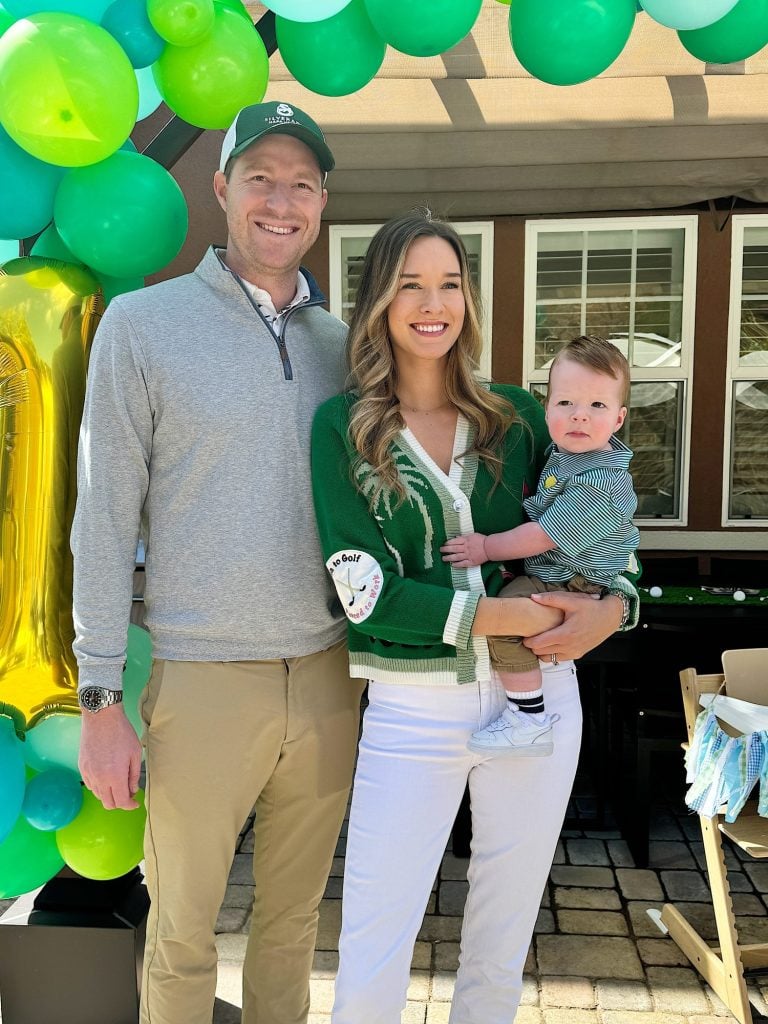 A family with a baby celebrating an event with green and blue balloons in the background.