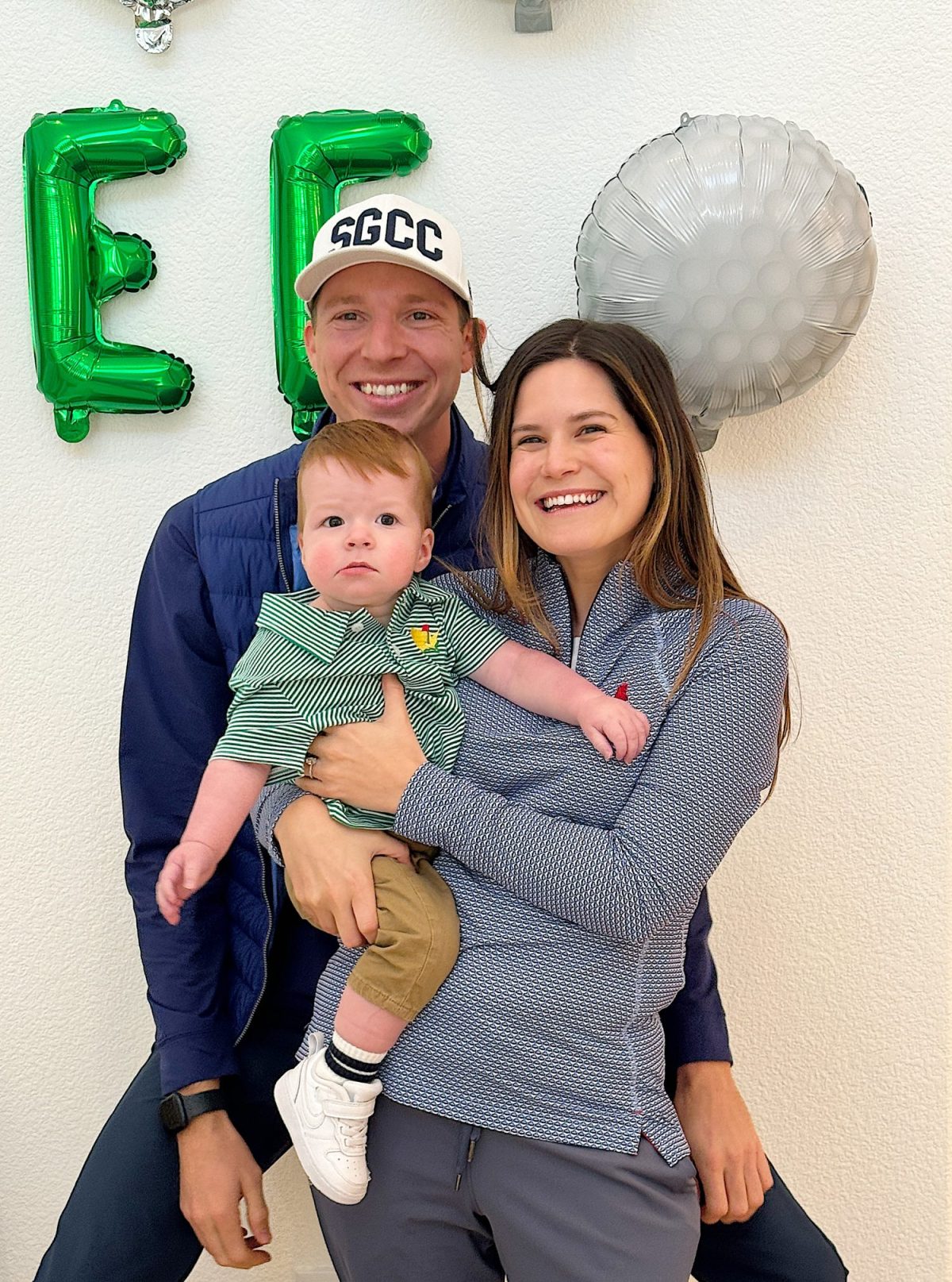 A couple with their nephew posing for a photo with letter balloons in the background.